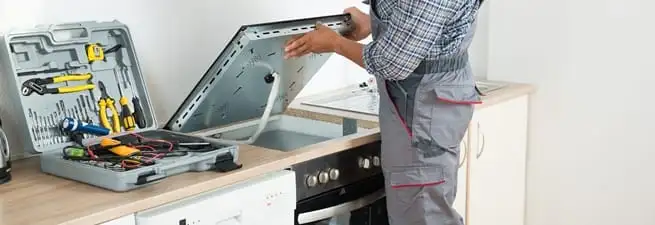 Cooktop repair technician lifting a built-in stovetop for service in Charleston, SC