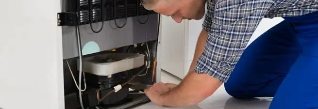 Refrigerator repair technician servicing the compressor and condenser area in Charleston, SC